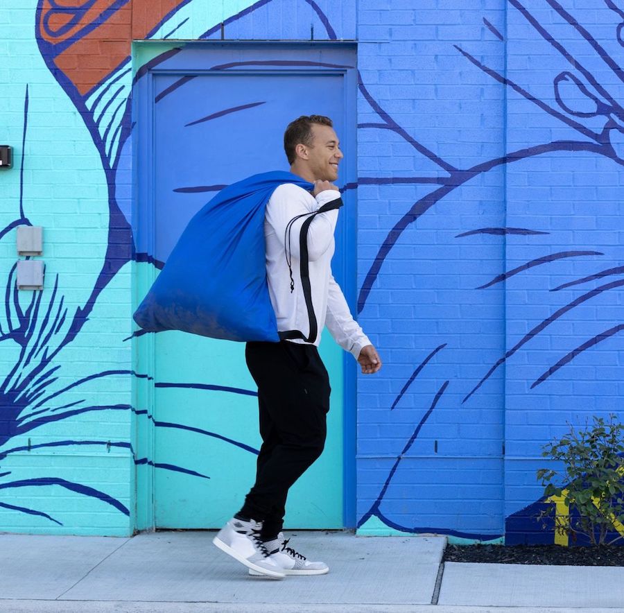 Carefree man with blue Push Laundry bag walking in front of a colorful mural